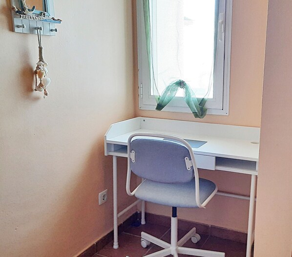 A small, white desk with a grey chair in a corner room with a window.