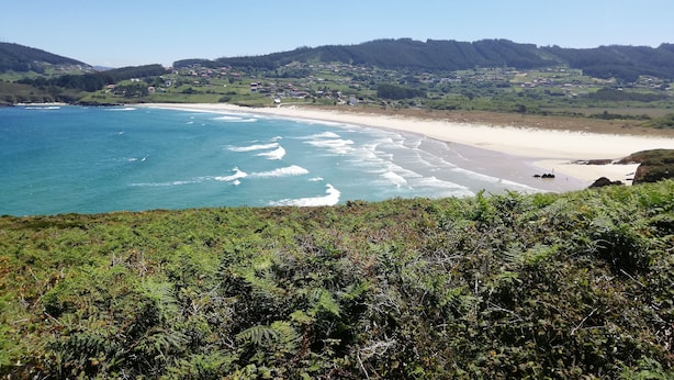 Un paysage côtier avec une plage, des vagues de l’océan et, en arrière-plan, des collines.