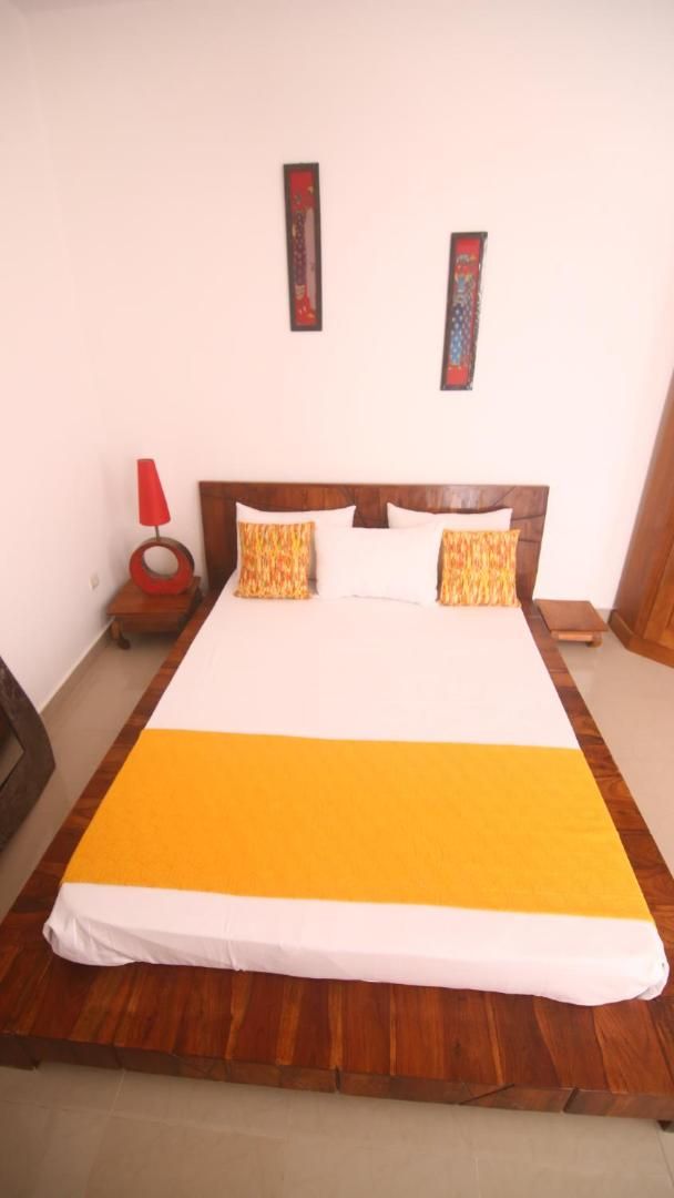 Una cama con cabecera de madera, ropa de cama blanca y amarilla, y dos almohadas decorativas.