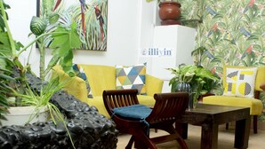 Ein Zimmer mit einem gelben Sofa, einem Holzstuhl, einem Couchtisch und mehreren Blumentöpfen.