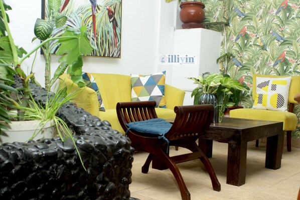 A room with a yellow sofa, a wooden chair, a coffee table, and various potted plants. - Hotel Illiyin (Dakar)