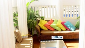 Ein gemütliches Wohnzimmer mit einem braunen Sofa, bunten Kissen, einem Glastisch und einer Topfpflanze.