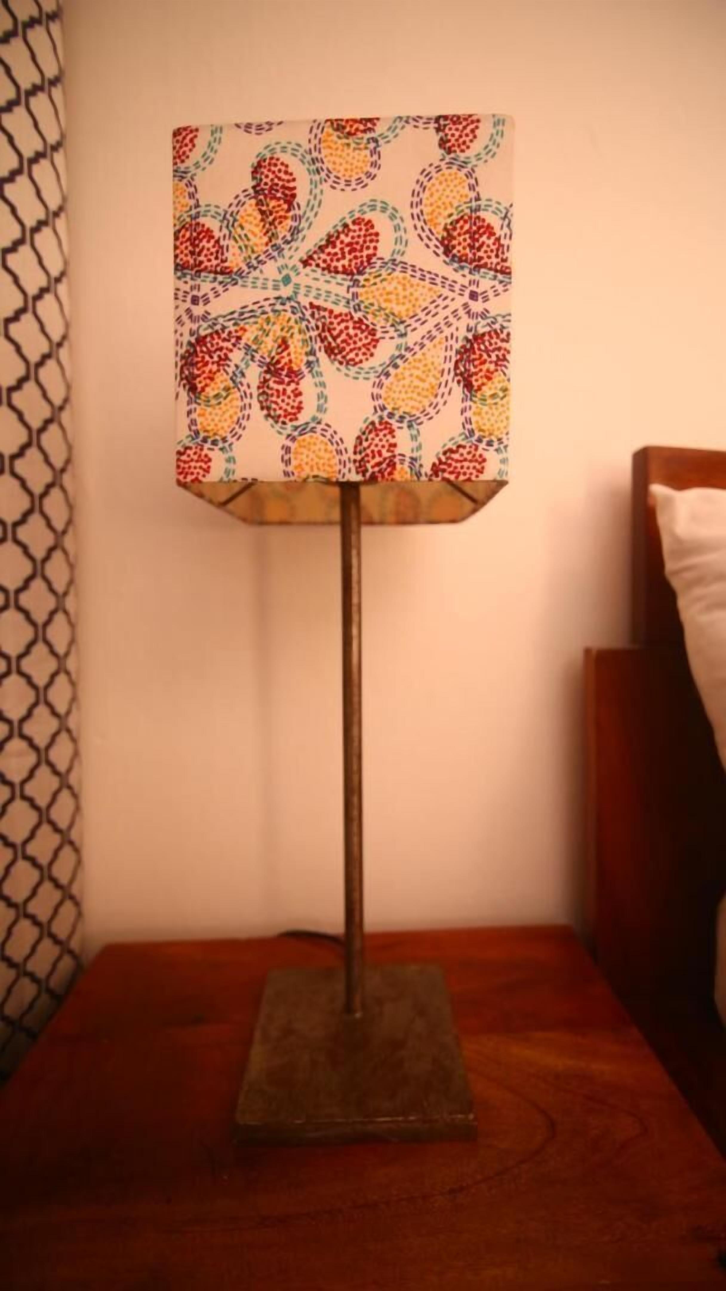 Een vloerlamp met een lantaarnkap met patroon op een nachtkastje van hout.