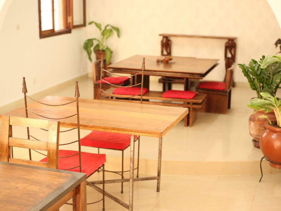 A dining area with wooden tables and chairs, red cushions, and potted plants.