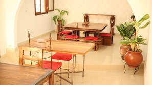 A dining area with wooden tables and chairs, red cushions, and potted plants. - Hotel Illiyin (Dakar)