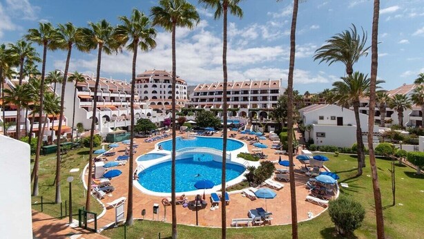 Un resort con piscina central rodeada de palmeras y tumbonas.