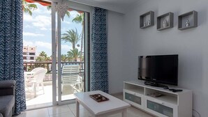 Una sala de estar moderna con televisor de pantalla plana, muebles blancos y un balcón con mobiliario exterior.