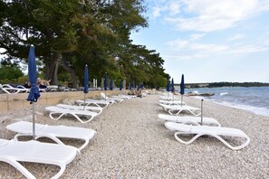 Een kiezelstrand met witte ligbedden en blauwe parasols, rijend geplaatst.