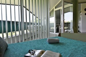 Hotelkamer met een bed, een raam met zonwering, een balkon met een stoel en uitzicht op de omgeving.