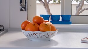 Un comptoir de cuisine blanc sur lequel se trouve un panier blanc contenant des oranges, un plateau bleu et une fenêtre donnant sur des arbres.