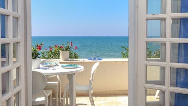 Une terrasse ouverte avec une table et des chaises, une vue sur la mer et des plantes en pot.
