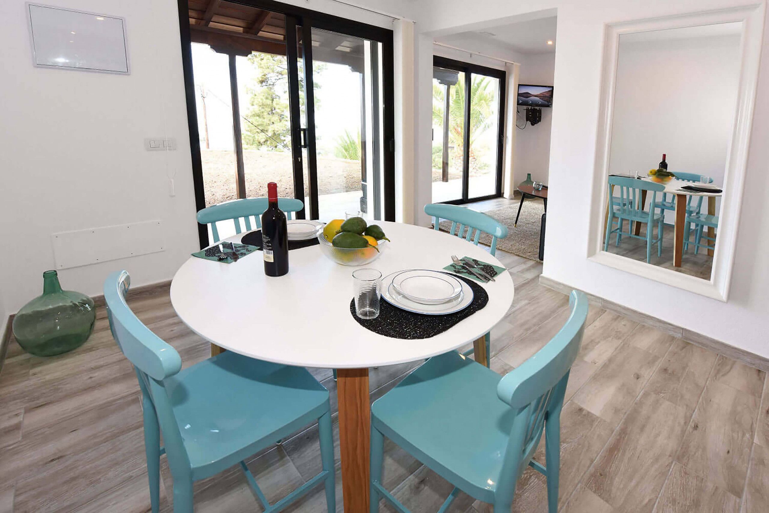 A dining area with a round table, four chairs, a bottle of wine, a bowl of fruit, and a glass.