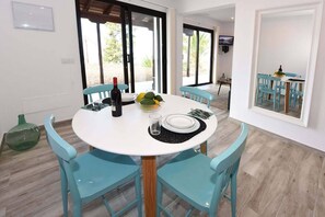 A dining area with a round table, four chairs, a bottle of wine, a bowl of fruit, and a glass.