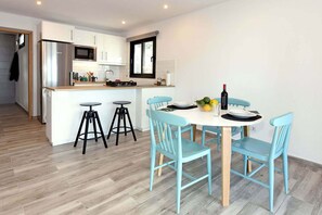A modern kitchen with white cabinets, a stainless steel refrigerator, and a microwave. There is a dining area with a round table and four blue chairs.