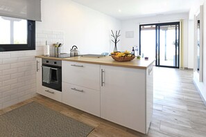 A modern kitchen with white cabinetry, a black oven, and a wooden countertop.