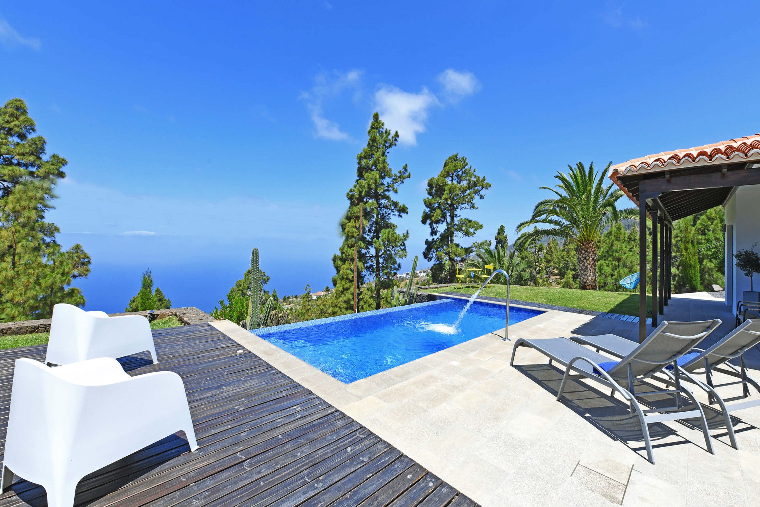 Una piscina con vista despejada al océano, rodeada de una terraza de madera y sillas de descanso.