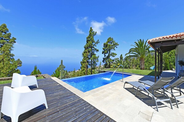 A pool with a clear view of the ocean, surrounded by wooden decking and lounge chairs.