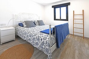 A bedroom with a bed, bedside table, lamp, window, and a wooden ladder.