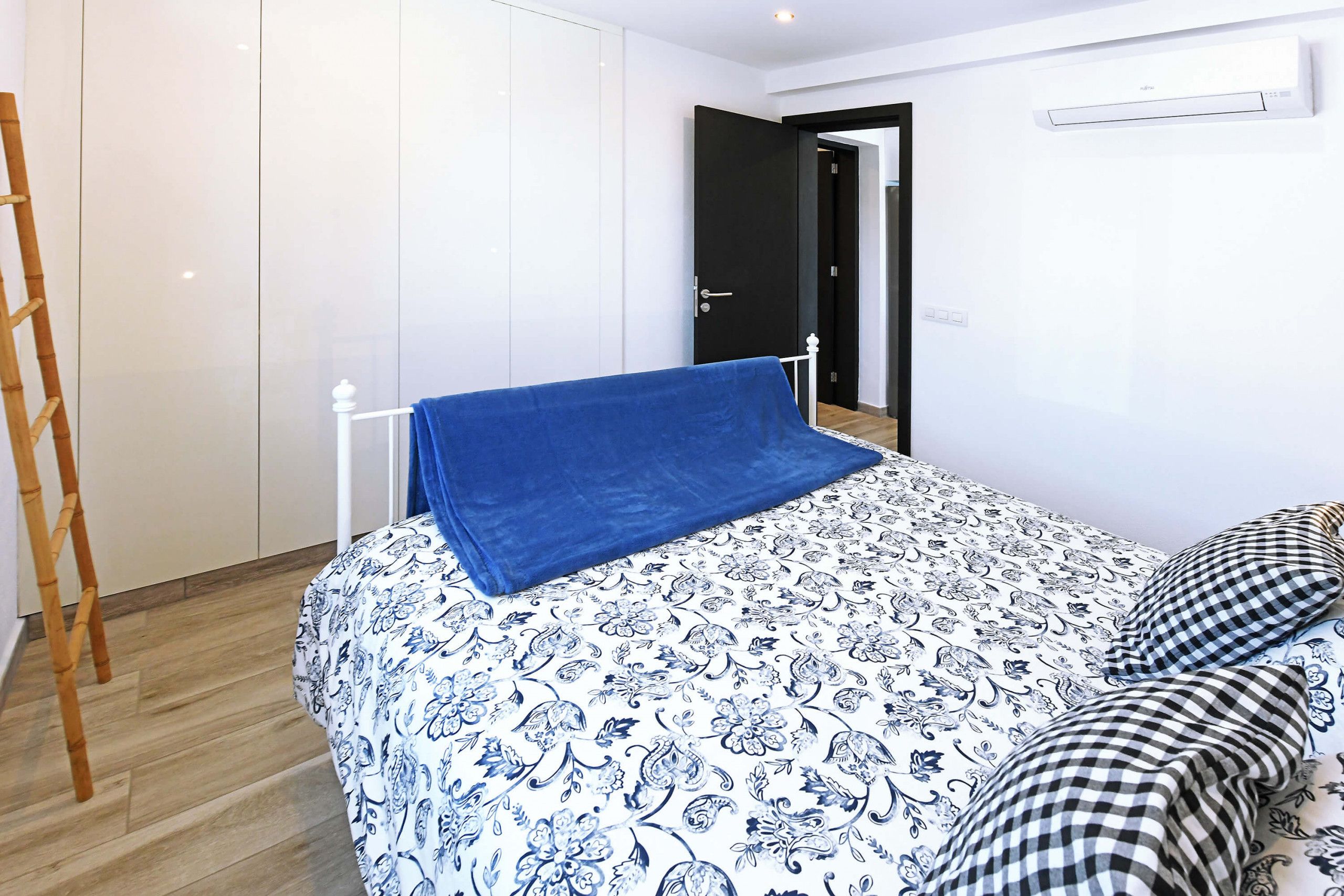 Un dormitorio con cama, una escalera de madera, una puerta negra y una pared blanca.