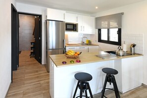 A modern kitchen with white cabinets, a stainless steel refrigerator, a microwave, a sink, and a window above the countertop.
