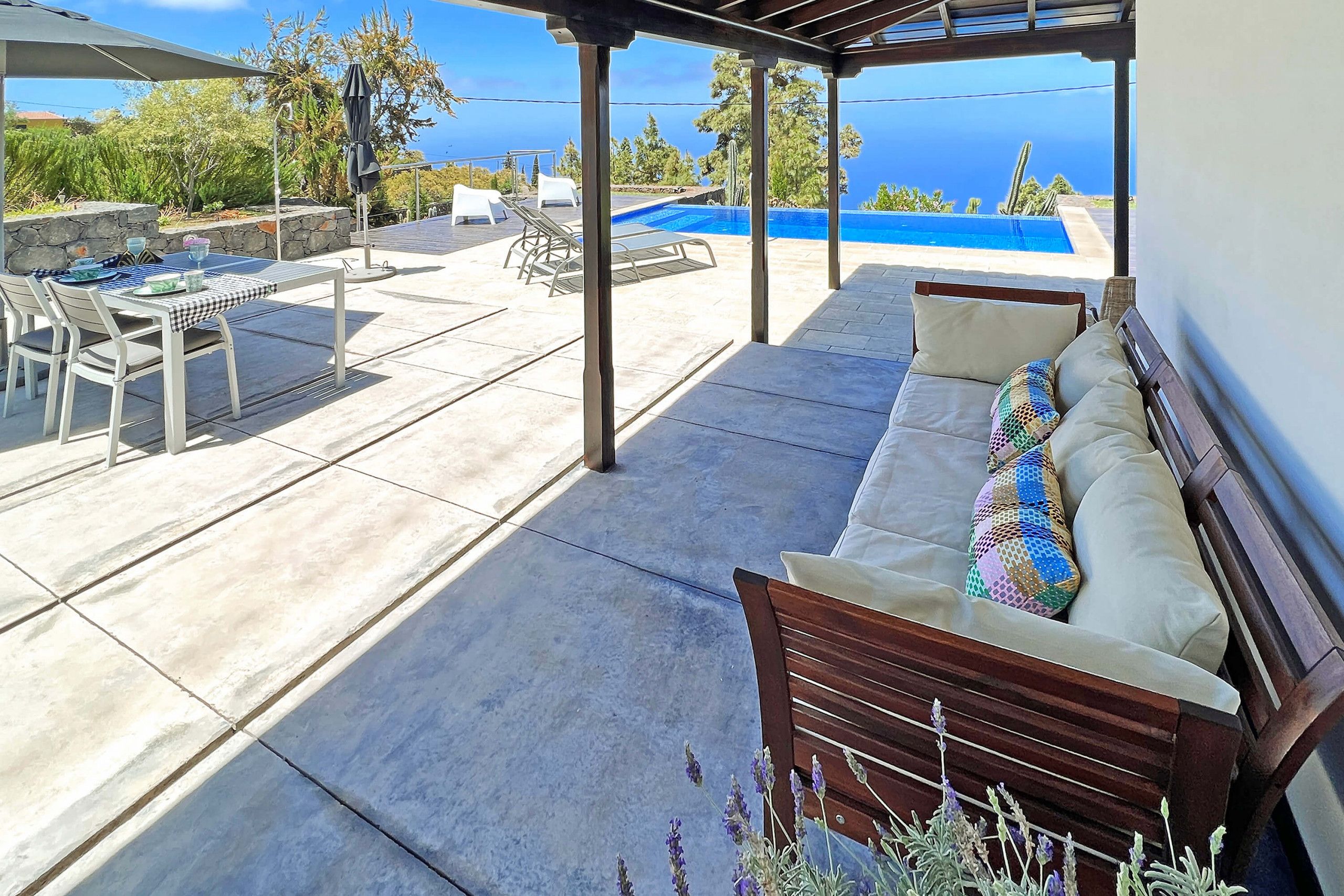 A covered outdoor area with a pool, seating, and a view of the sea.