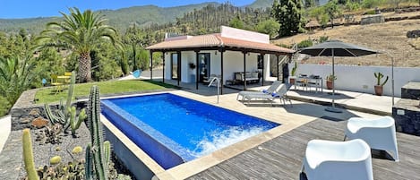 Un espace piscine extérieur moderne, doté d’un coin salon couvert, de chaises longues et offrant une vue sur un paysage montagneux.