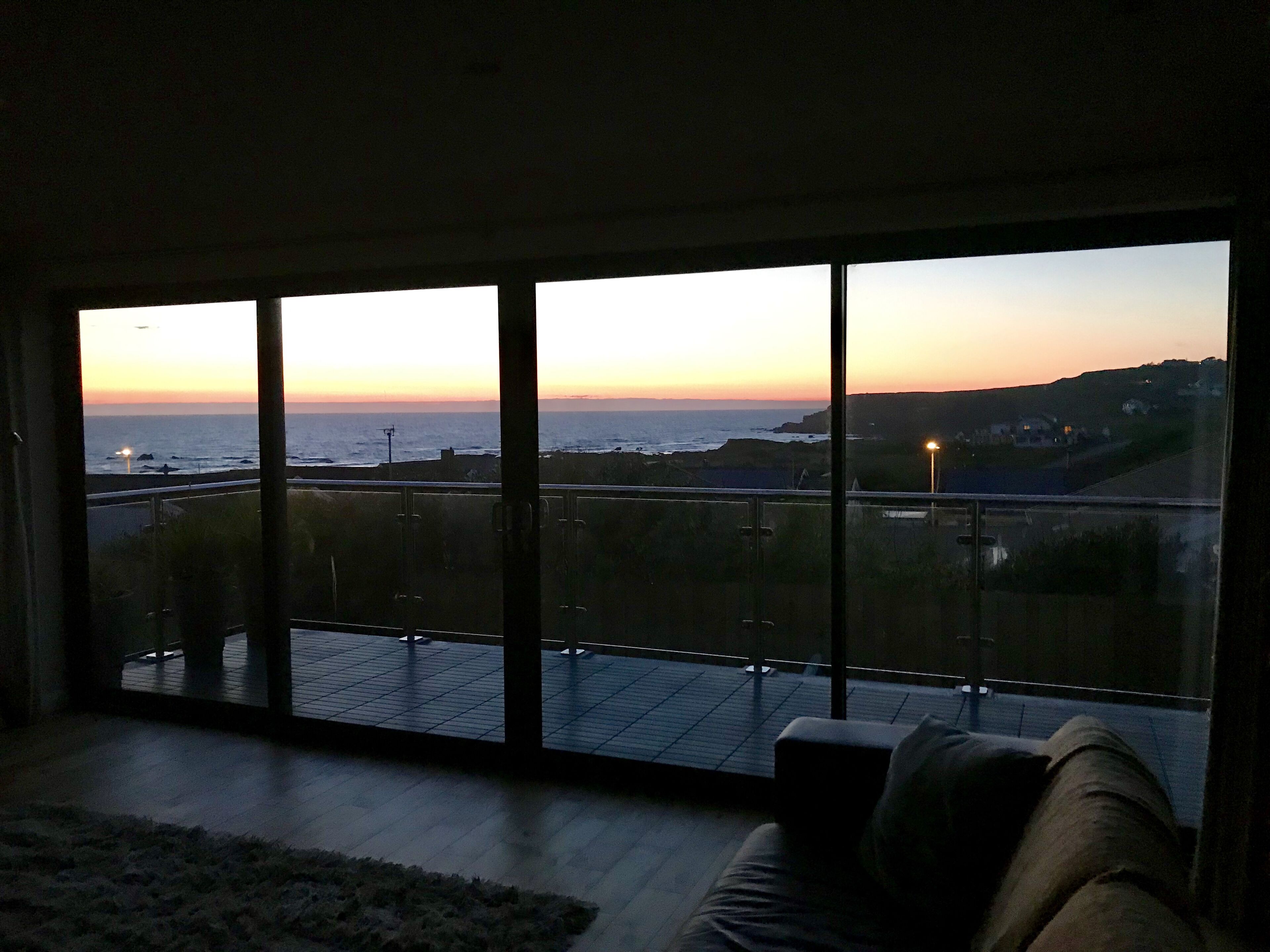 A room with large windows overlooking a coastal view at sunset.