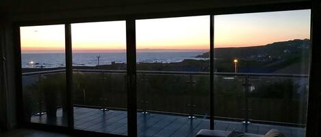 A room with large windows overlooking a coastal view at sunset.
