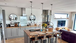Een moderne keuken met een centraal eiland, barstoelen en een eettafel. Een groot raam zorgt voor natuurlijk licht en uitzicht op de omgeving.