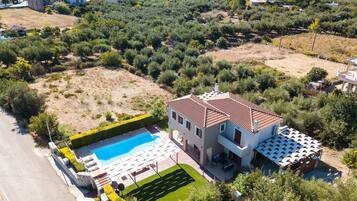 An aerial view of a residential property with a swimming pool, a well-maintained garden, and a large house with a tiled roof.