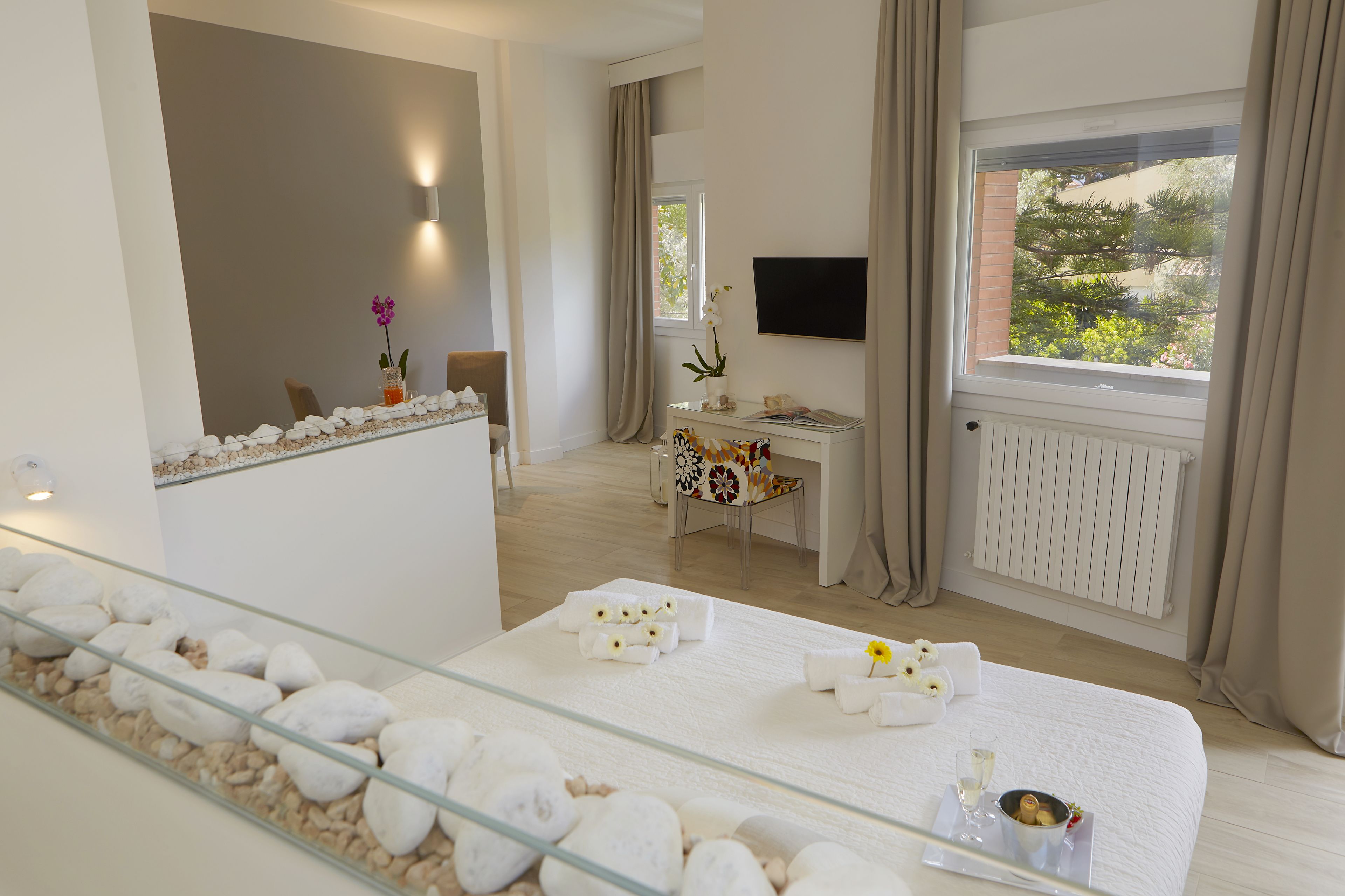 Habitación de hotel con cama, escritorio, televisión y ventana con vistas a árboles.