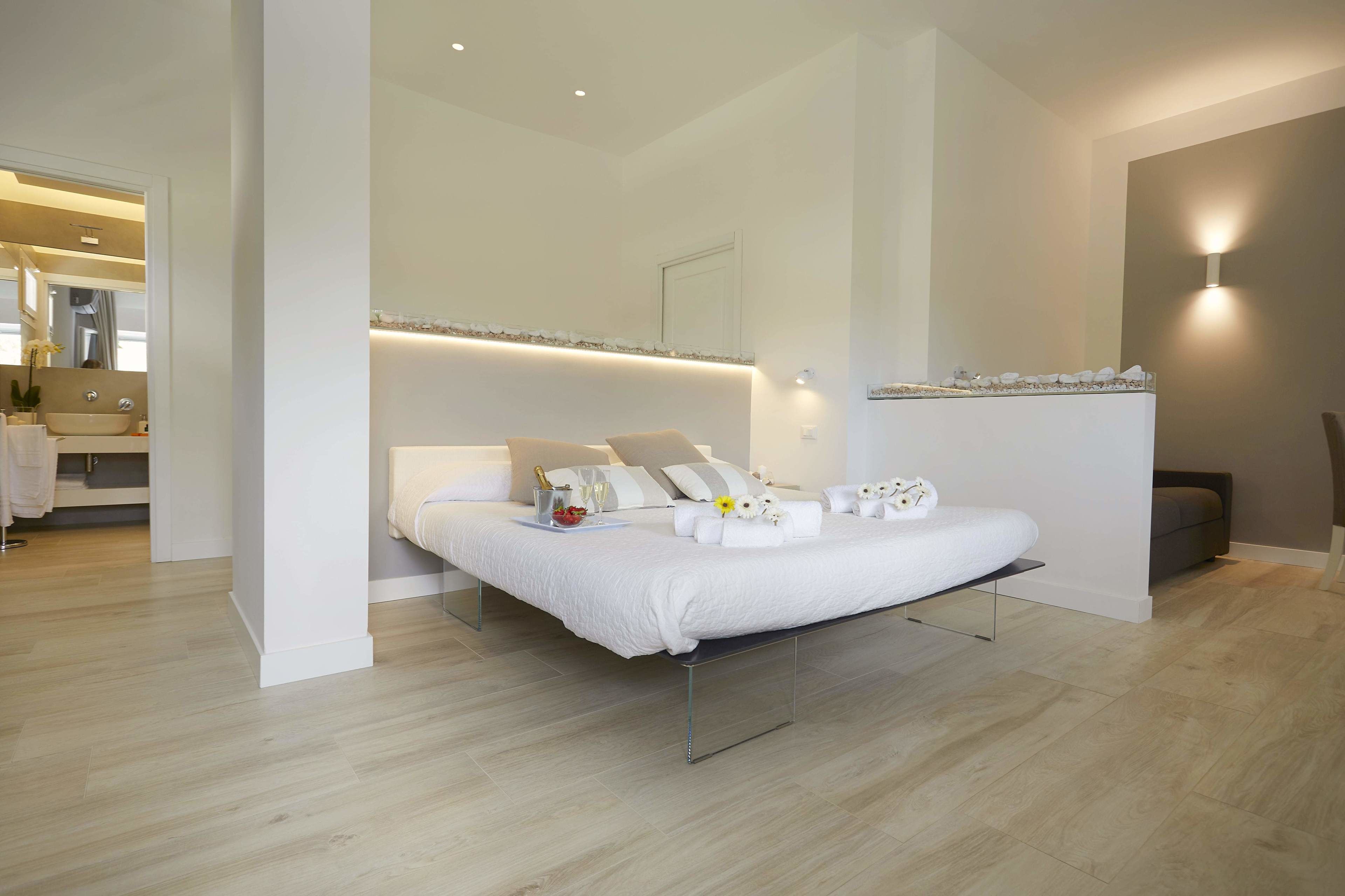 A modern bedroom with a large bed, a bedside table with a glass of water and a bottle, and a nightstand with a lamp.