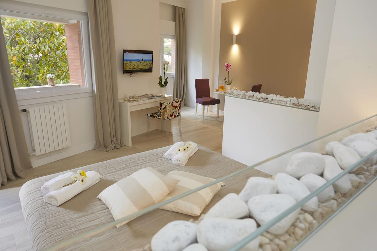 Habitación de hotel con cama, escritorio, silla, televisor y baño con ducha de vidrio.
