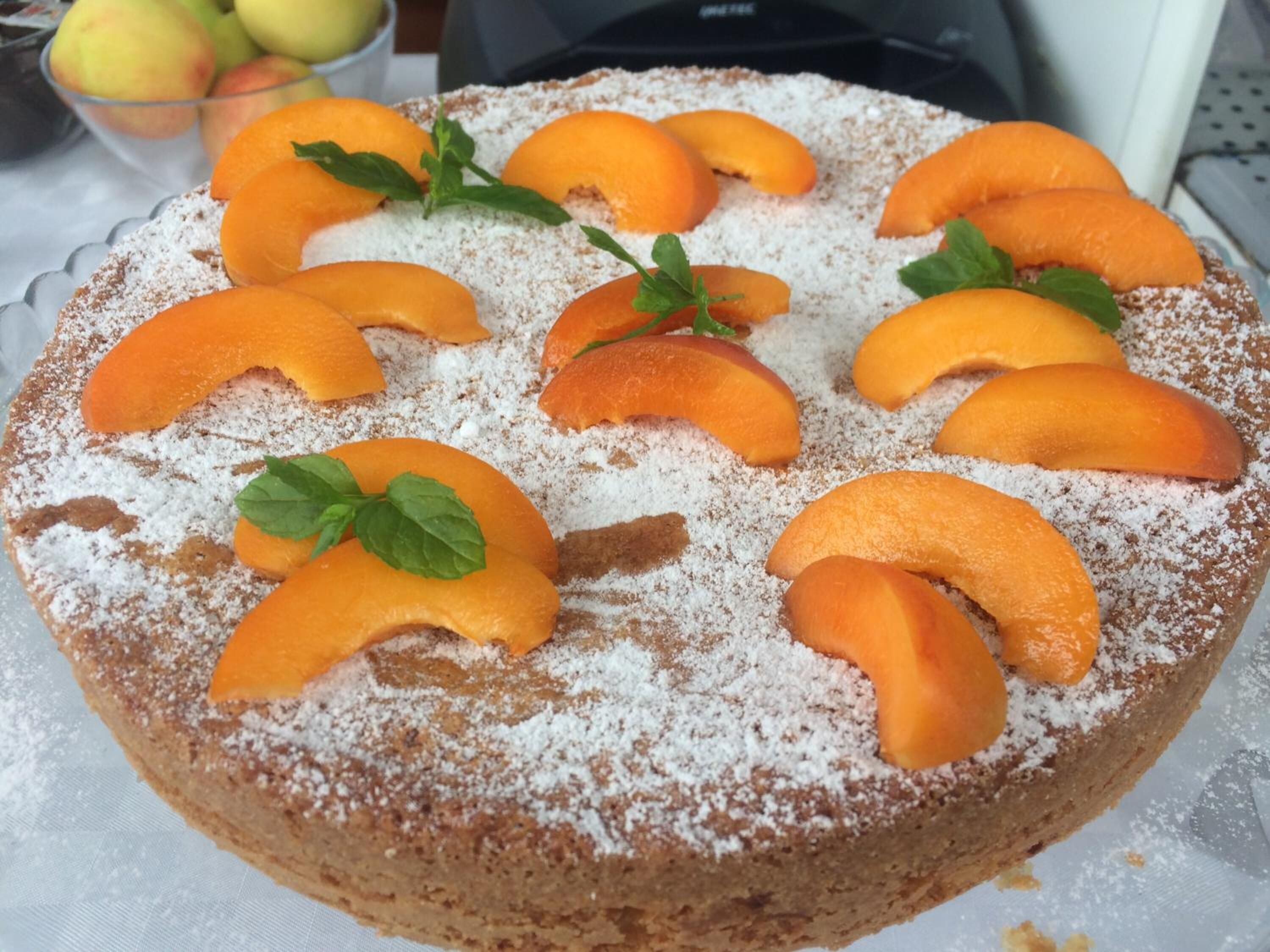 Un gâteau rond, garni de tranches de pêches et de feuilles de menthe, et saupoudré de sucre glace.
