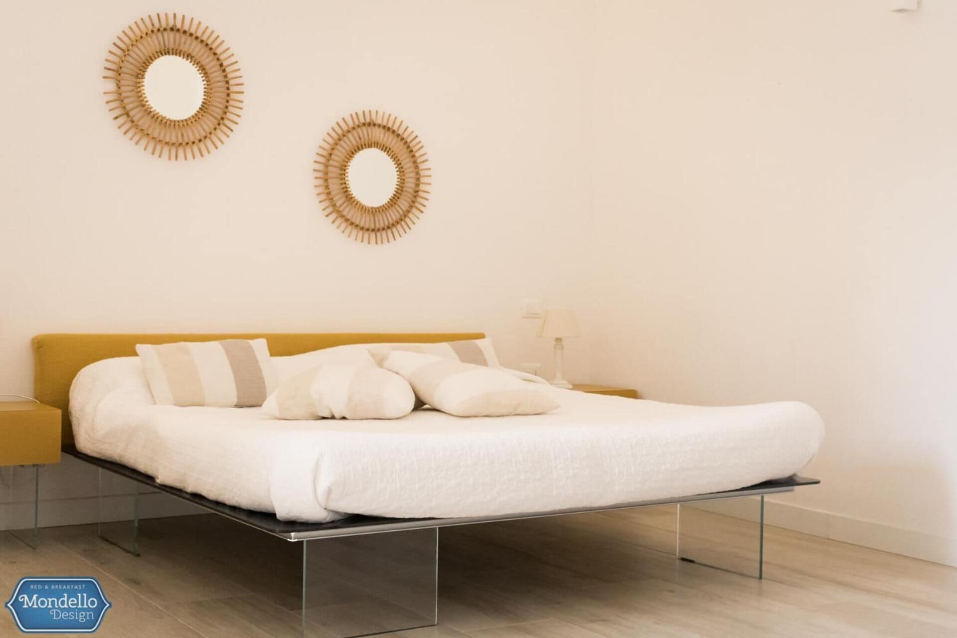 A modern bedroom with a bed, two wall-mounted circular mirrors, and a bedside table with a lamp.