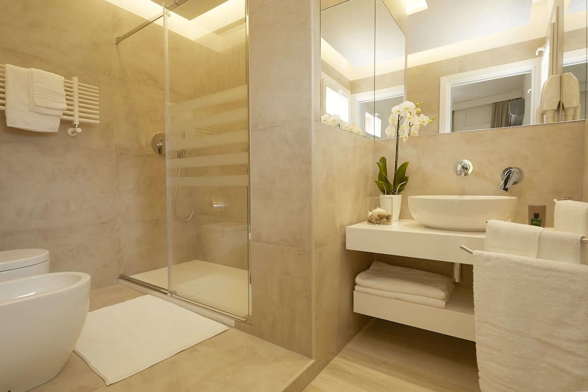 Un baño moderno con ducha envuelta en vidrio, un lavamanos blanco y un espejo grande.