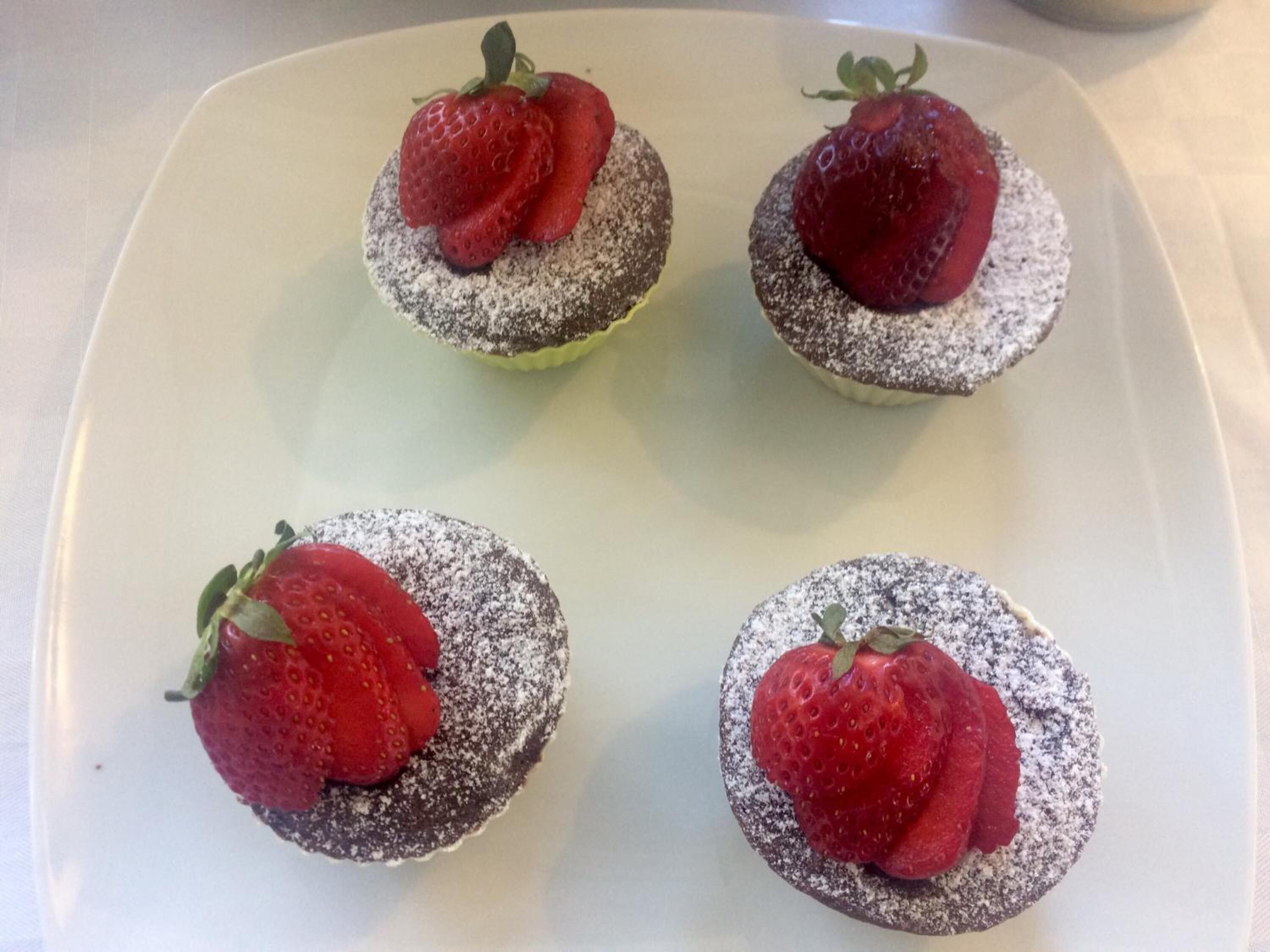 Quattro cupcakes al cioccolato con fragole su un piatto bianco.