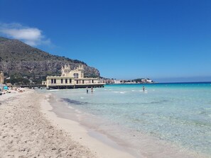 Una playa con agua turquesa cristalina, una orilla de arena y un edificio de arquitectura clásica al fondo.