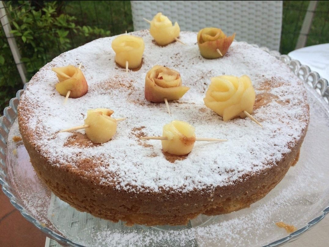 A round cake with powdered sugar and decorative roses on skewers, placed on a glass cake stand.
