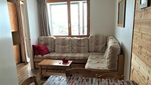 A cozy room with a wooden floor, a sofa with patterned cushions, a small table, and a window with curtains.