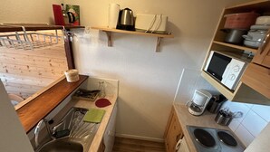 A compact kitchen with a sink, stove, microwave, and wooden shelves.