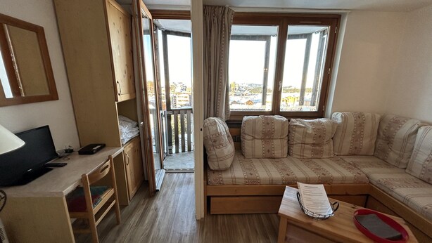 A compact living space with a wooden desk, a sofa, and a view of the outside.
