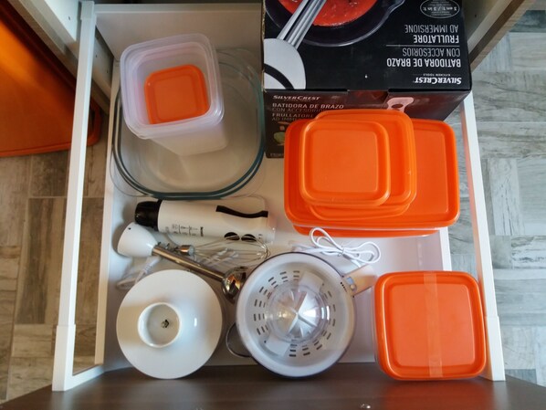 Un cajón con utensilios de cocina, incluyendo recipientes naranja y blanco, un colador y un plato blanco.