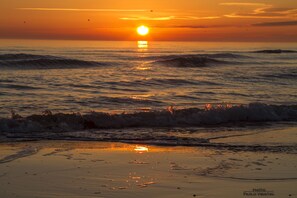 Una playa al atardecer con olas y un sol visible.