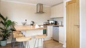Una cocina moderna con una isla central, taburetes de bar, lavavajillas integrado y una planta en maceta.