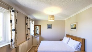 Un dormitorio con cama de madera, una mesita de noche, un radiador, un espejo y dos cuadros en la pared.