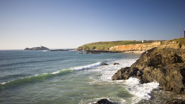 Un paisaje costero con costas rocosas, un faro y una isla distante.