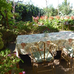 An outdoor garden setting with a table covered by a floral tablecloth, surrounded by metal chairs. - Charming 2-Bedroom Apartment for 4 Guests (Veli Lošinj)