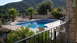 A rectangular swimming pool with a stone border, surrounded by a black metal fence. There are lounge chairs and a palm tree in the pool area. -  Luxury Air Conditioned Villa Close to Calonge Centre - Fantastic Views (Calonge)