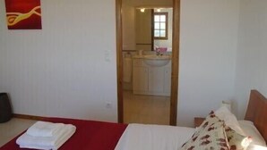 A bedroom with a bed, a red blanket, and a white pillow. There is a door leading to a bathroom with a sink and mirror. -  Luxury Air Conditioned Villa Close to Calonge Centre - Fantastic Views (Calonge)